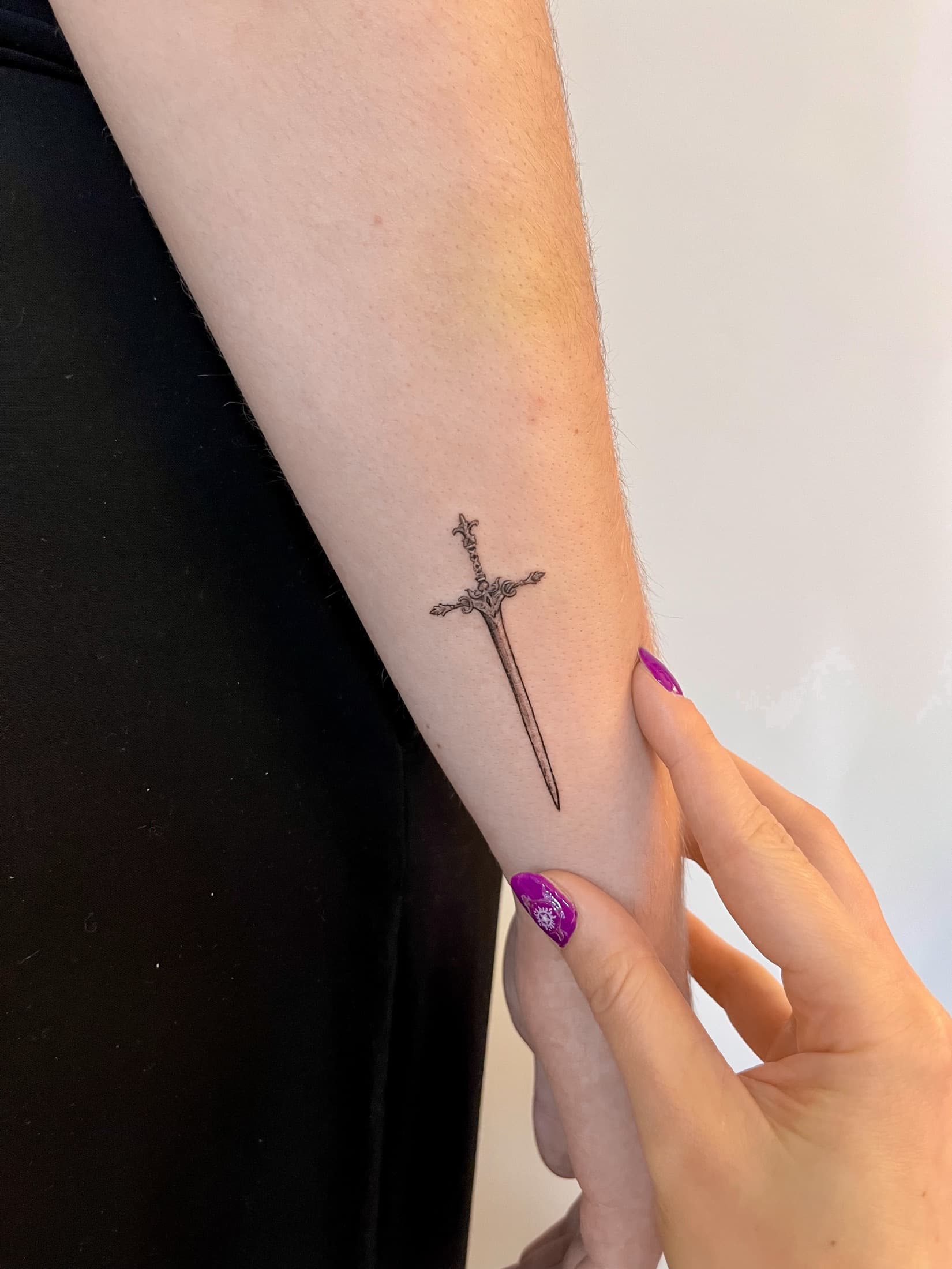 Minimalist sword tattoo on the forearm