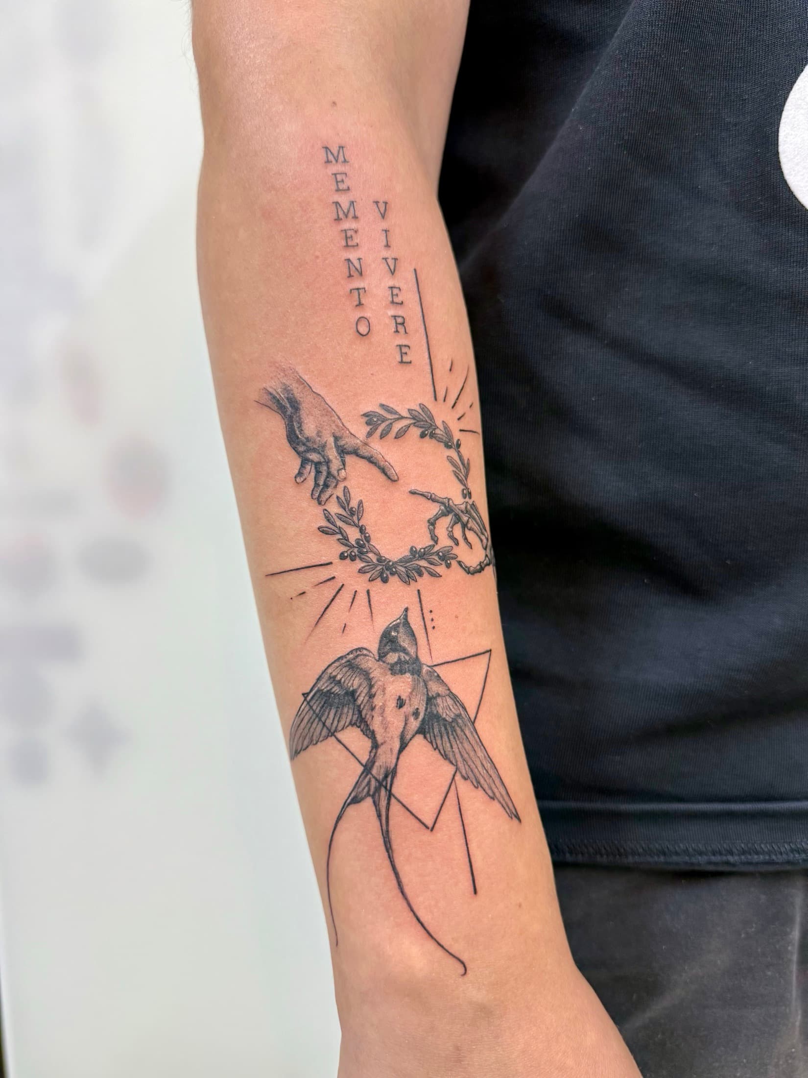 Forearm tattoo with Memento Vivere lettering, hands and a swallow